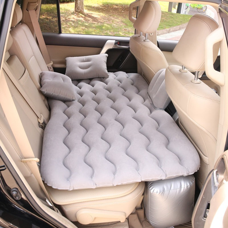 Gray car inflatable mattress set up in the back seat of a car, with pillows placed on it, ready for use.